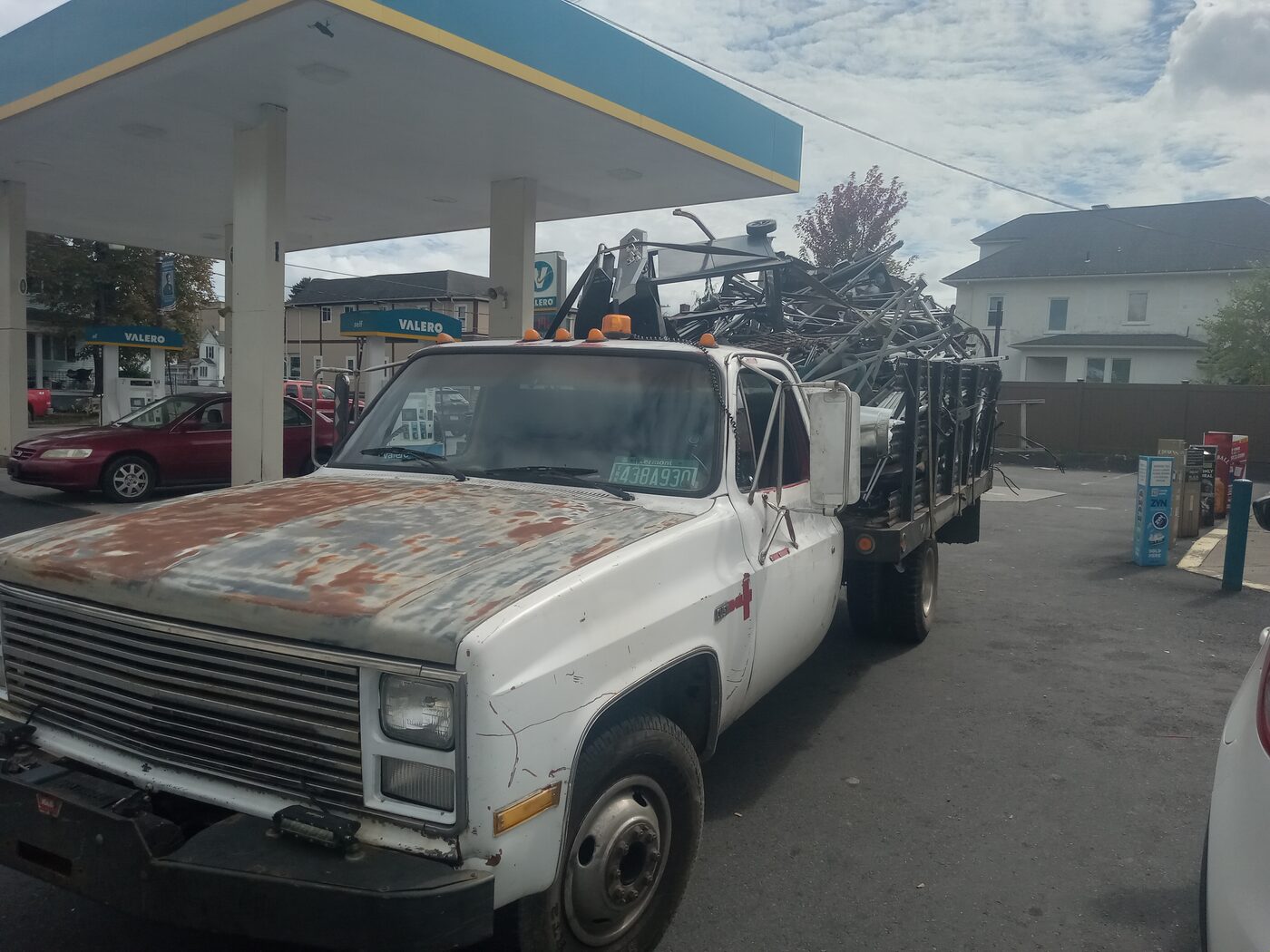 Rusty white flatbed truck loaded with scrap metal at a Valero gas station