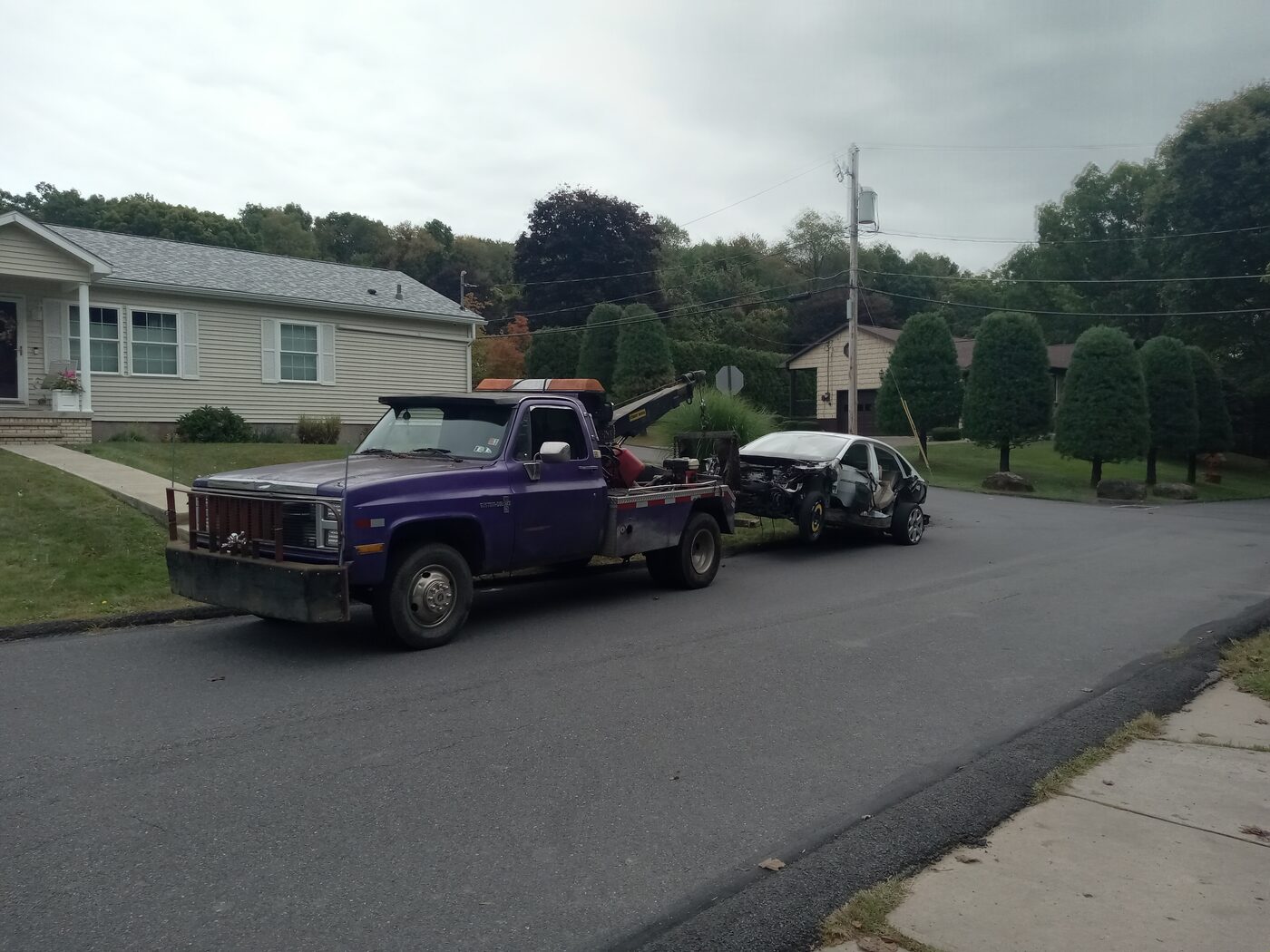 Tow truck towing a wrecked sedan down a residential street