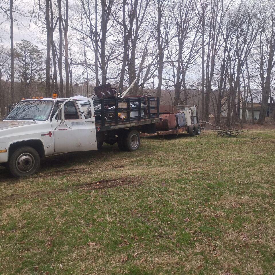 Flatbed truck and loaded trailer parked at the tree line after a scrap pickup